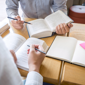 People holding pencils over open books at a table