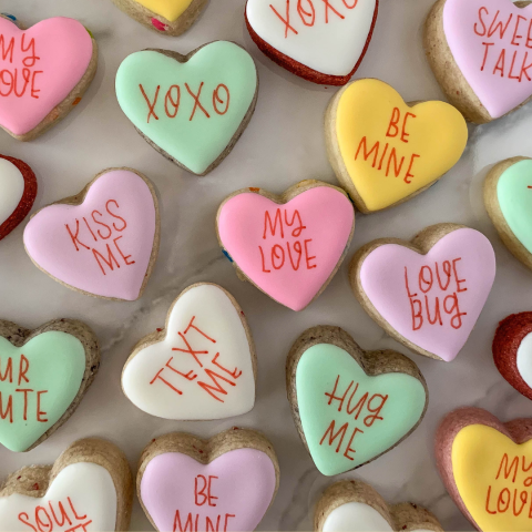 Frosted sugar cookies shaped and decorated like conversation heart candies.