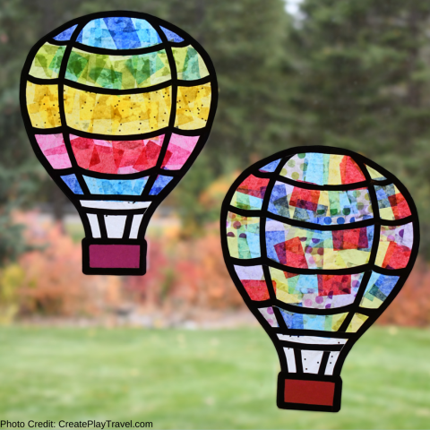 Two colorful hot air balloon suncatchers made with black outlines and colorful paper against a window showing an outdoor background out of focus