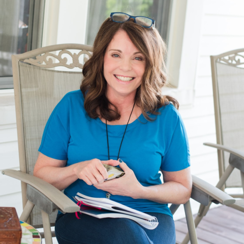 woman sits in a chair on a porch holding tarot cards and smiling