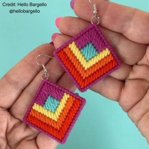 A pair of diamond shaped multicolored yarn earrings held in a person's hands