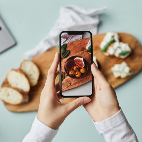 Two white hands holding a smart phone and taking a picture of food. Blue background. 