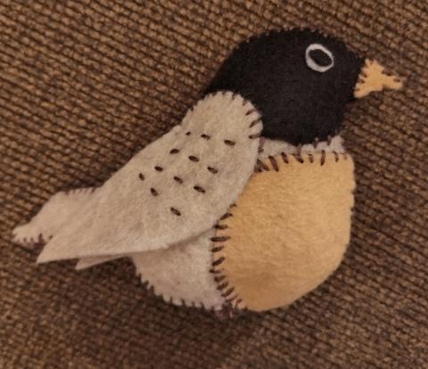 Bird made of felt sewed together on a brown background. 