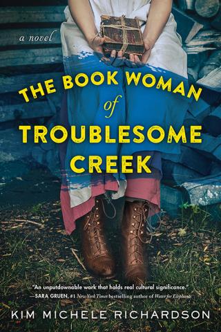 The cover of The Book Woman of Troublesome Creek by Kim Michele Richardson. A woman in an old-fashioned dress holding books sits on stairs.