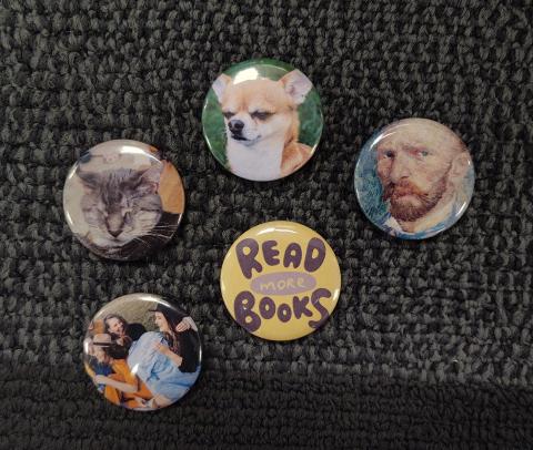 Five custom magnets on a dark carpet background. Each magnet has a different image (i.e. a dog, a cat, Van Gough, people, and a magnet with a yellow background and purple text that reads "Read More Books."