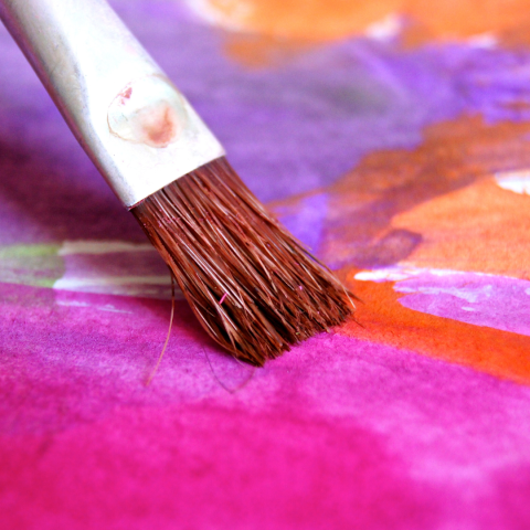 Paintbrush painting a colorful background of purple, magenta, orange, and brown.