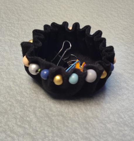 Small black bowl made of felt with decorative beads filled with paperclips and other small office supplies. 