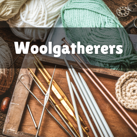 Yarn, knitting needles and crochet needles lie haphazard on a wood table.