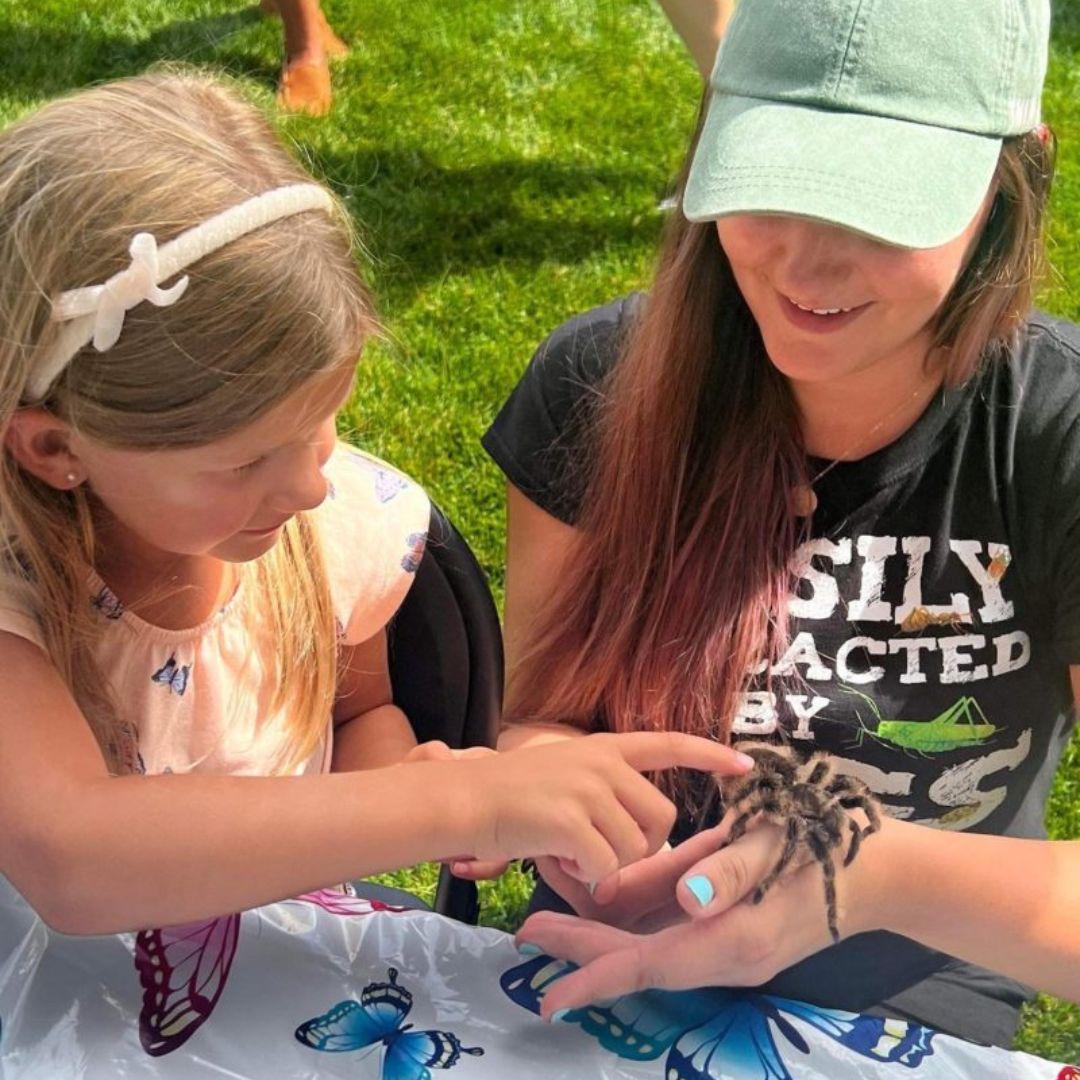 Image of Nadia holding a tarantula while a young girl touches it.