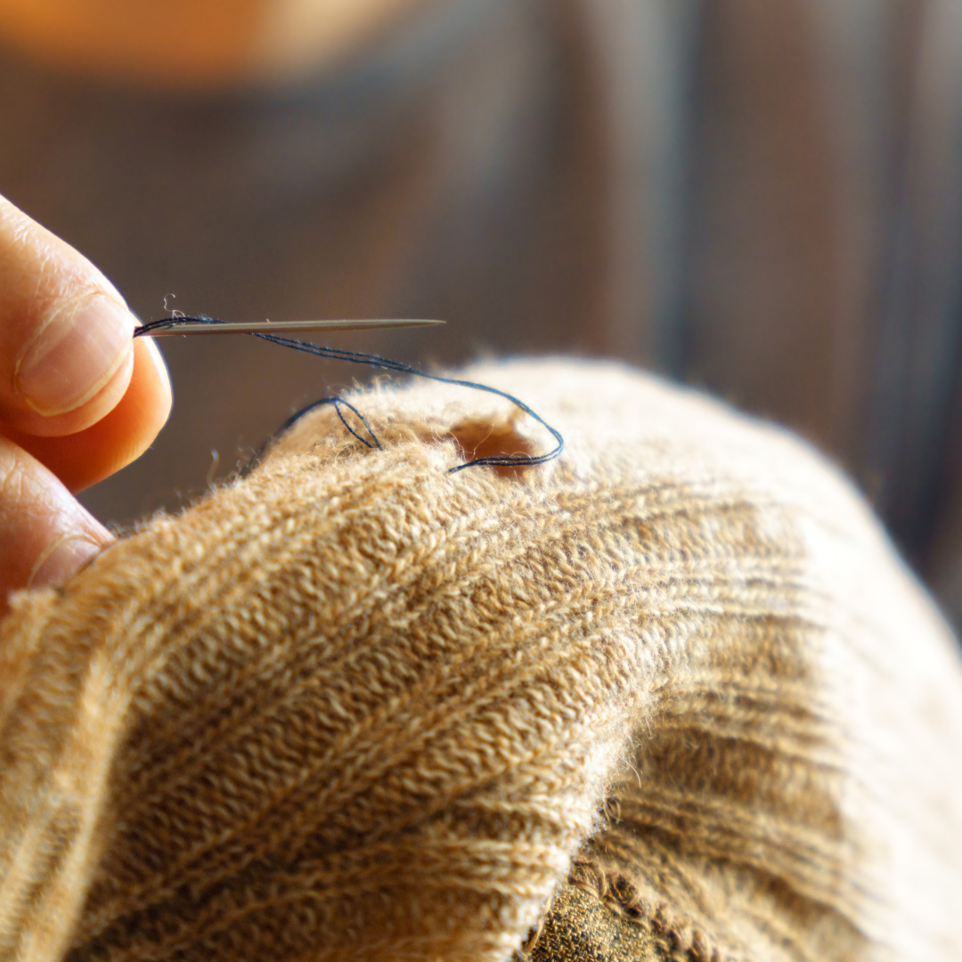 White fingers mending hole in yellow garment.