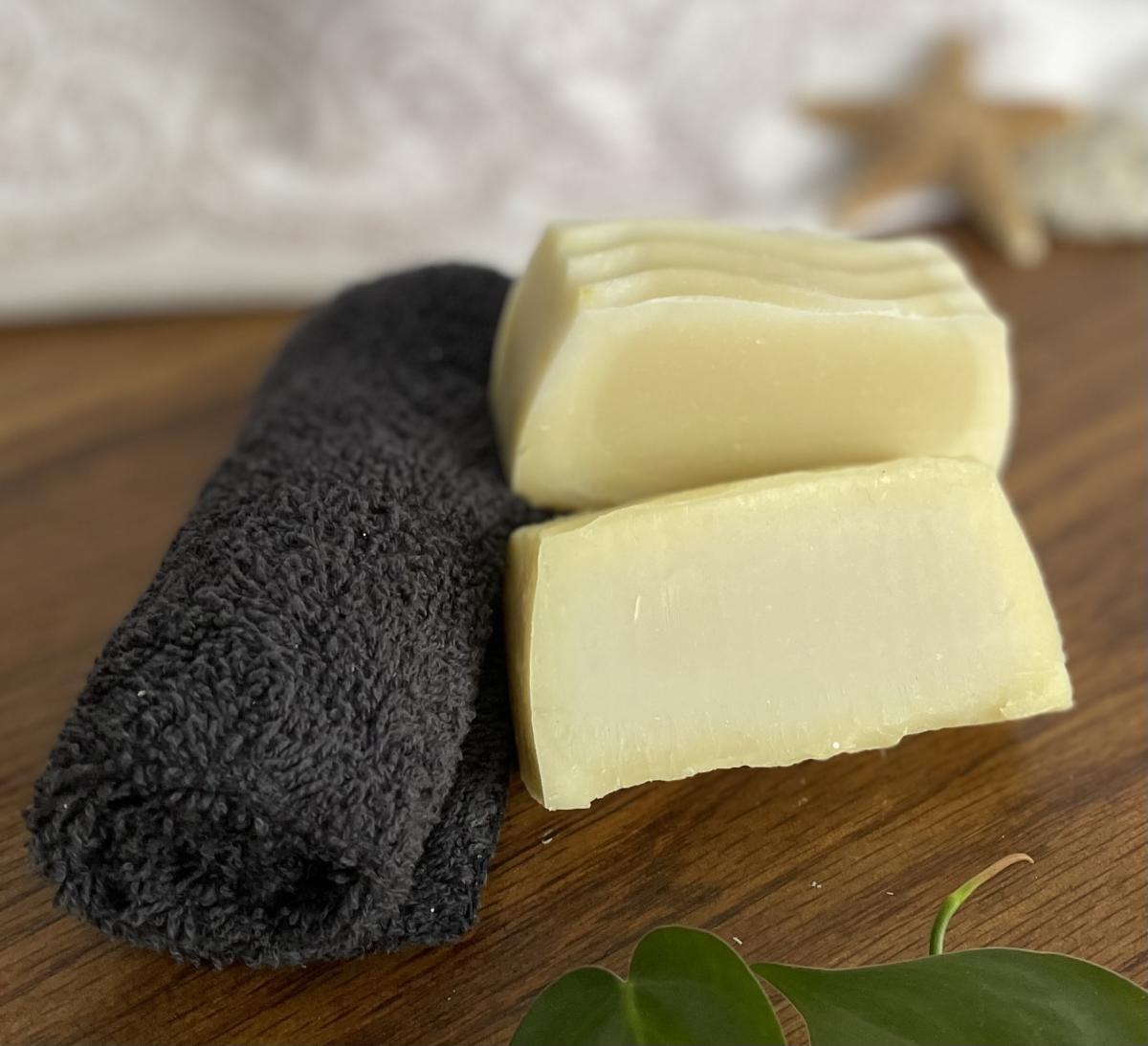 Bars of yellow homemade soap on a wooden table with a gray rolled up towel next to them. 