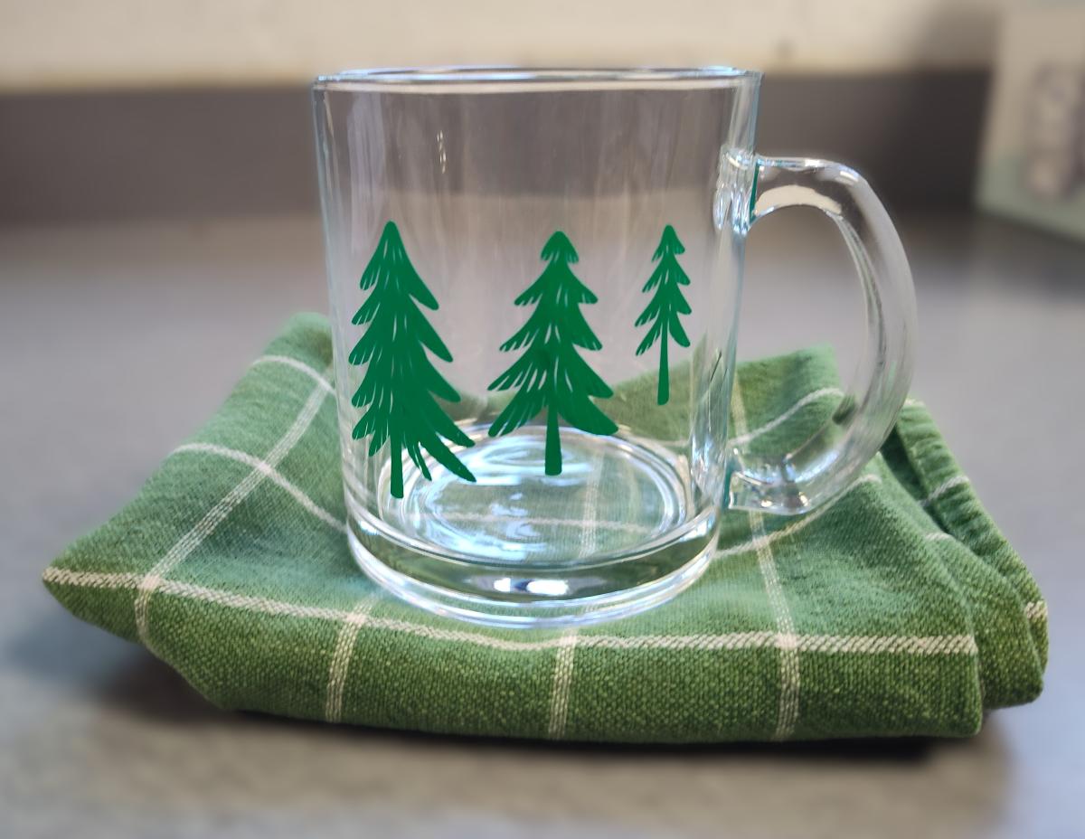 Glass mug with green tree vinyl decal on top of green dishcloth. 